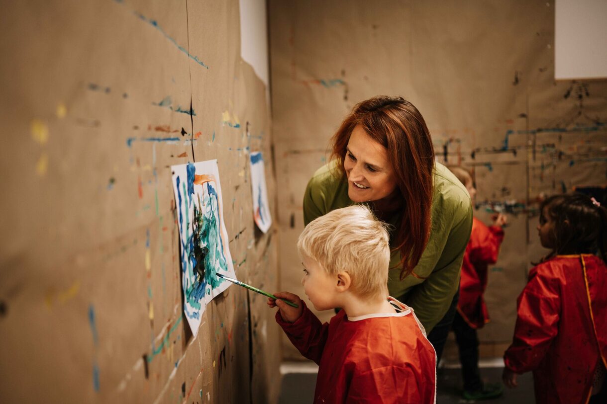 Eine Frau schaut einem Kind beim Malen zu