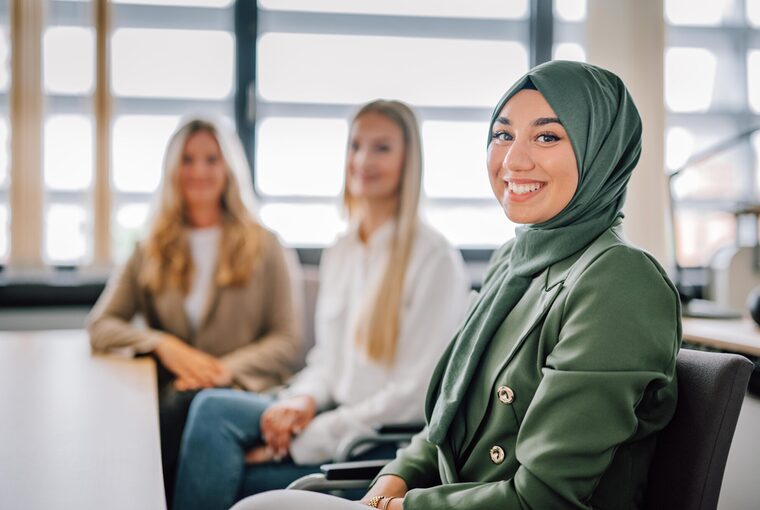 Drei weibliche Personen sitzen am Tisch und lachen in die Kamera