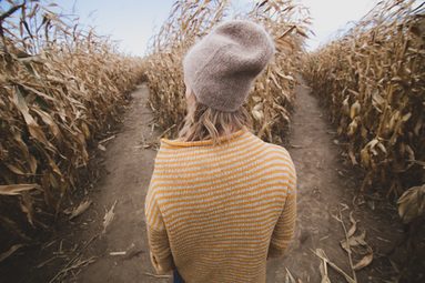 Mädchen steht im Maisfeld vor einer Weggabelung