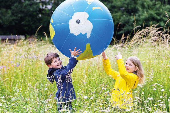 Zwei Kinder werfen sich auf dem Naturgut Ophoven einen großen Erdball zu