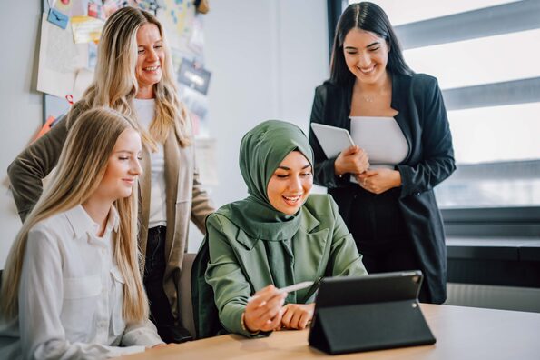 Vier Frauen sitzen und stehen vor einem Tisch und schauen auf ein Tablet