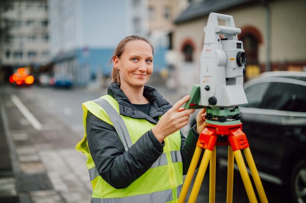 Eine Frau in Warnweste steht vor einem Vermessungsgerät