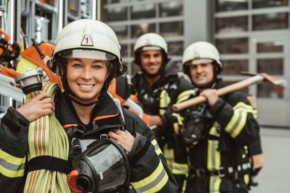 Drei Feuerwehrleute stehen mit Ausrüstung vor der Feuerwache