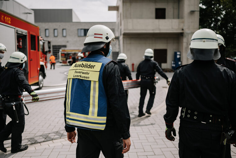 Feuerwehrmänner gehen zusammen auf ein Gebäude zu, einige tragen eine Leiter