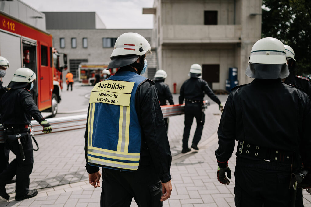 Feuerwehrmänner gehen zusammen auf ein Gebäude zu, einige tragen eine Leiter