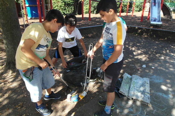 Drei Kinder sammeln Müll mit einer Müllzange