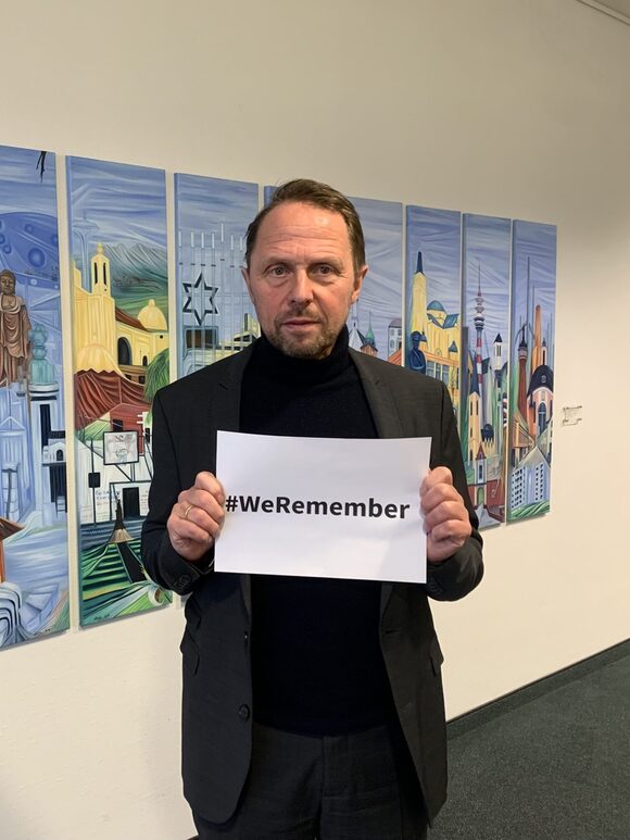 Oberbürgermeister Richrath hält ein Schild mit dem Hashtag We Remember in den Händen