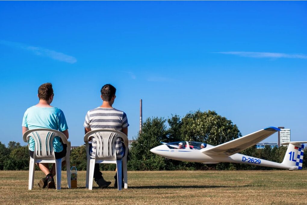 Zwei Zuschauer auf Stühlen beobachten den Start eines Flugzeugs