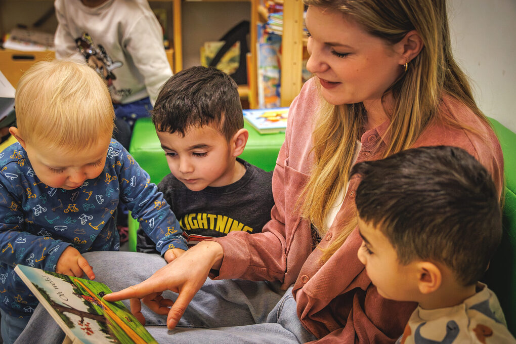 Eine Frau liest drei Kindern aus einem Buch vor