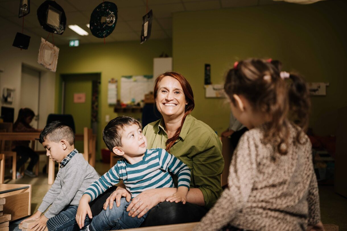 Eine Frau sitzt lächelnd mit drei Kindern zusammen