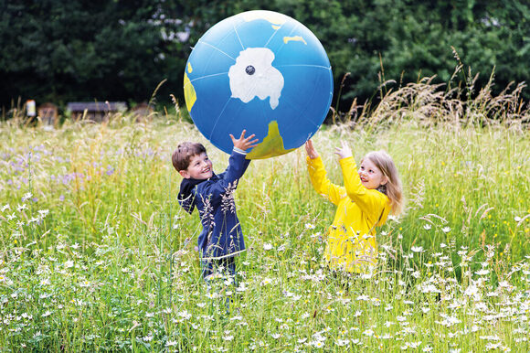 zwei Kinder halten einen Erdball auf einer Blühwiese im NaturGut Opoven