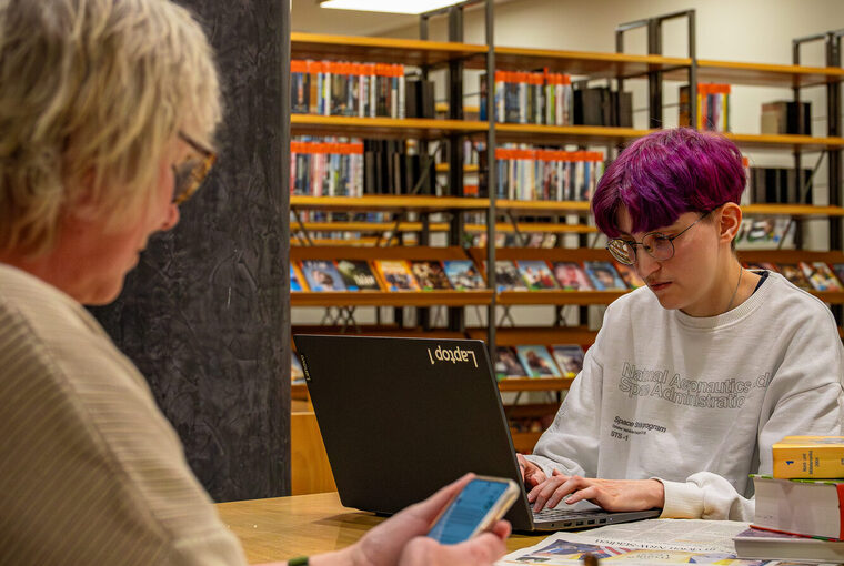 Zwei Personen sitzen am Tisch und arbeiten an Laptop und Smartphone