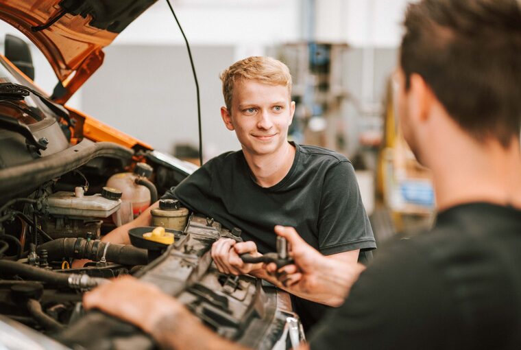 Zwei Personen arbeiten an einer Motorhaube vom Auto