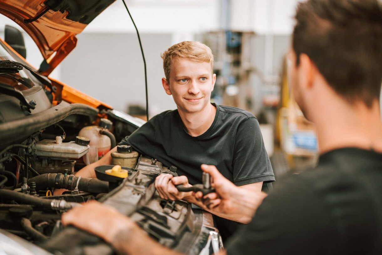 Zwei Personen arbeiten an einer Motorhaube vom Auto