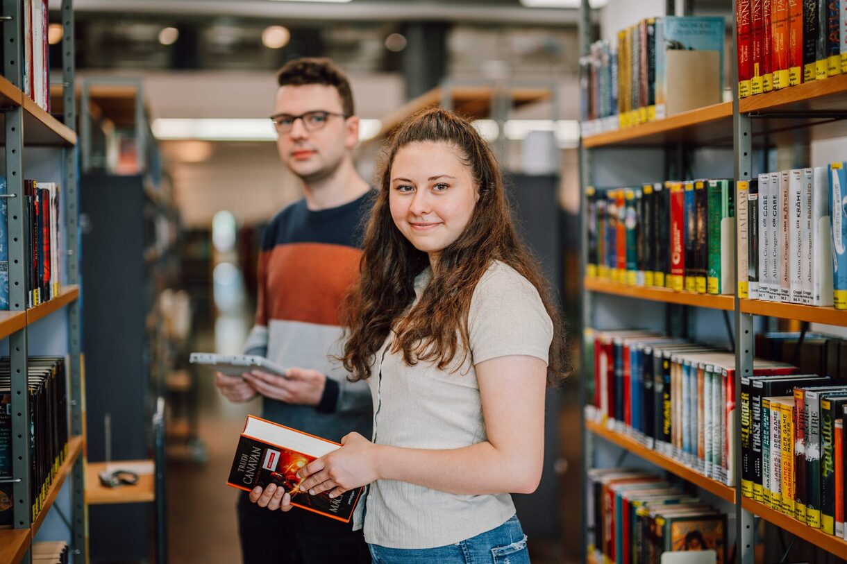 Zwei junge Personen stehen vor einem Bücherregal